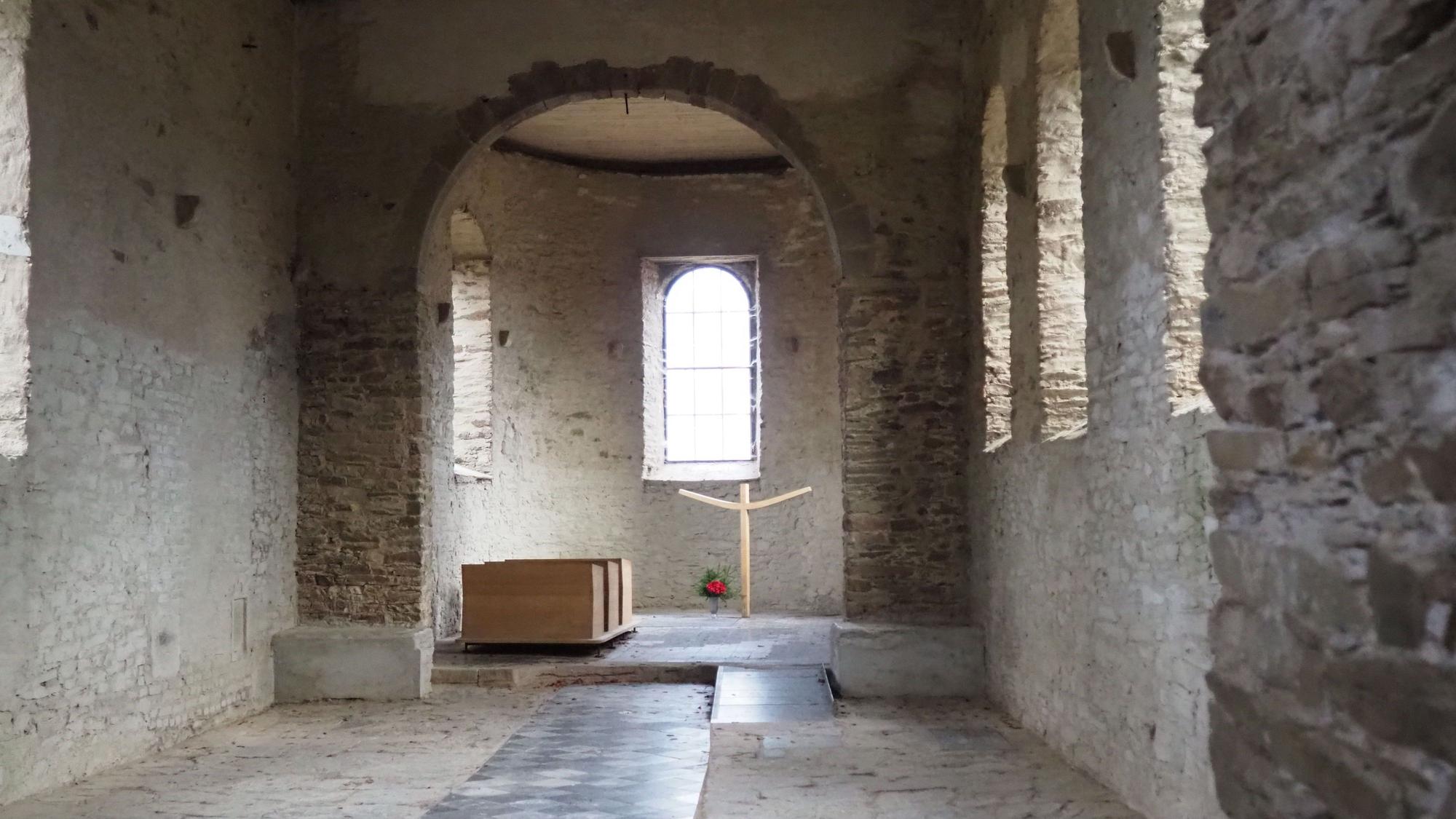 Blick in den Kirchenraum, mit Bogenfenstern und einem sehr modernen Kruzifix.