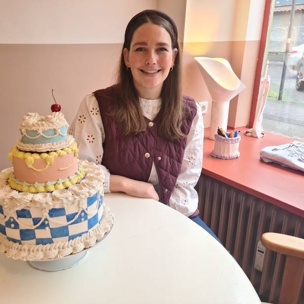 Eine junge Frau mit langem dunklem Haar sitzt an einem Tisch, auf dem ein Tortenmodell steht.