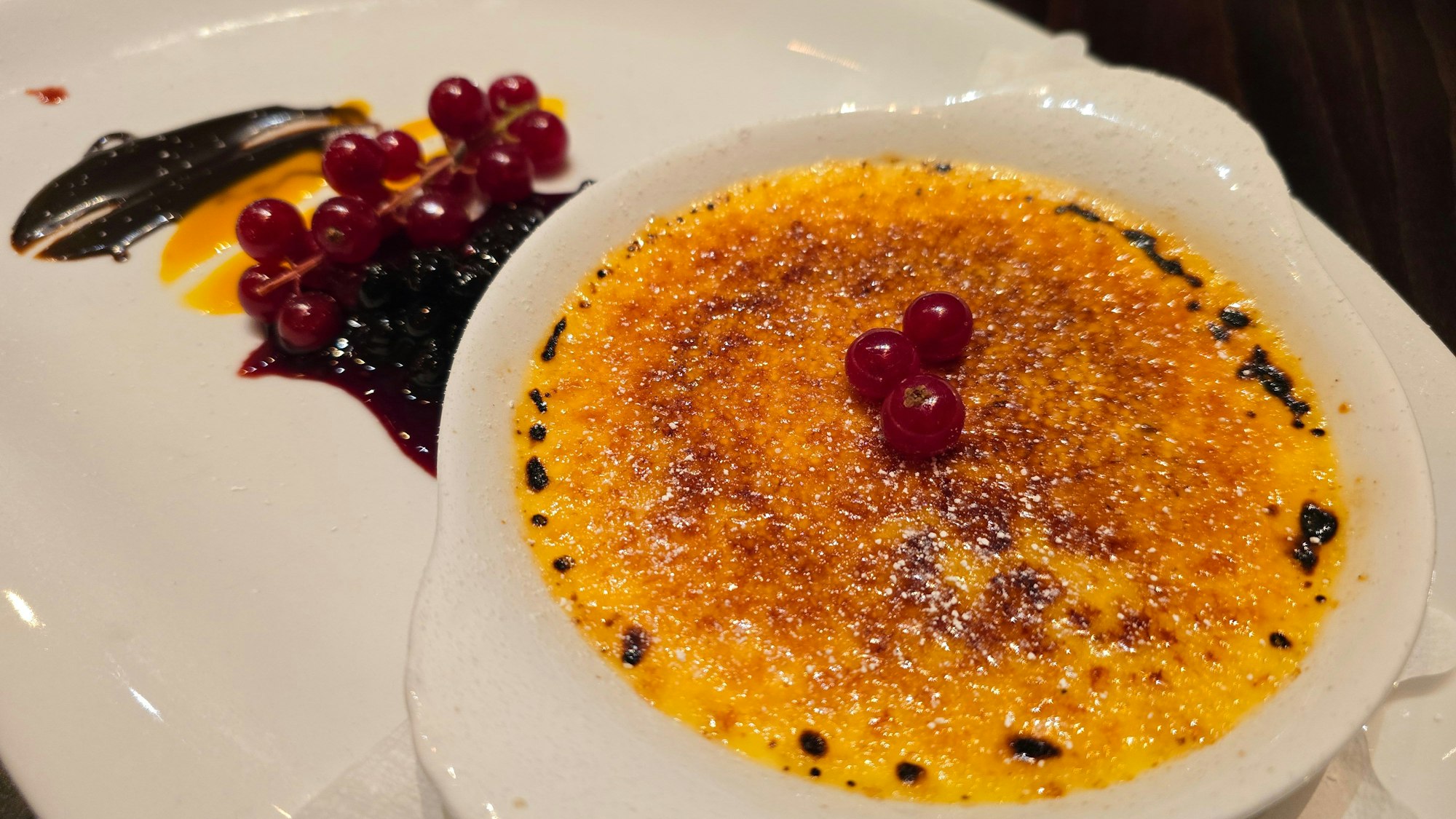 Das Dessert ist mit Johannisbeer-Deko auf weißem Geschirr zu sehen.