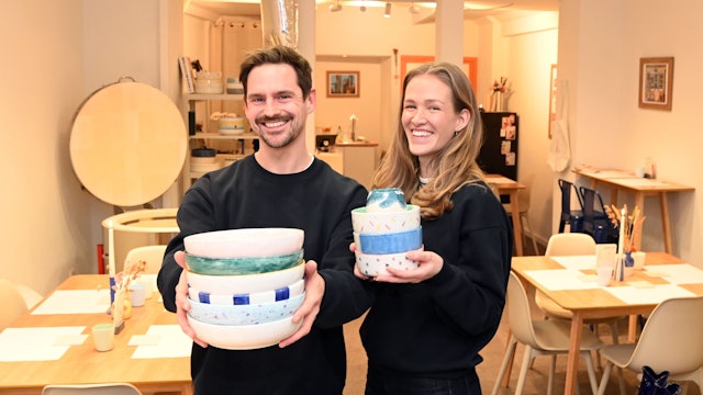 Ein Mann und eine Frau halten Keramik in die Kamera. Im Hintergrund sieht man Tische.