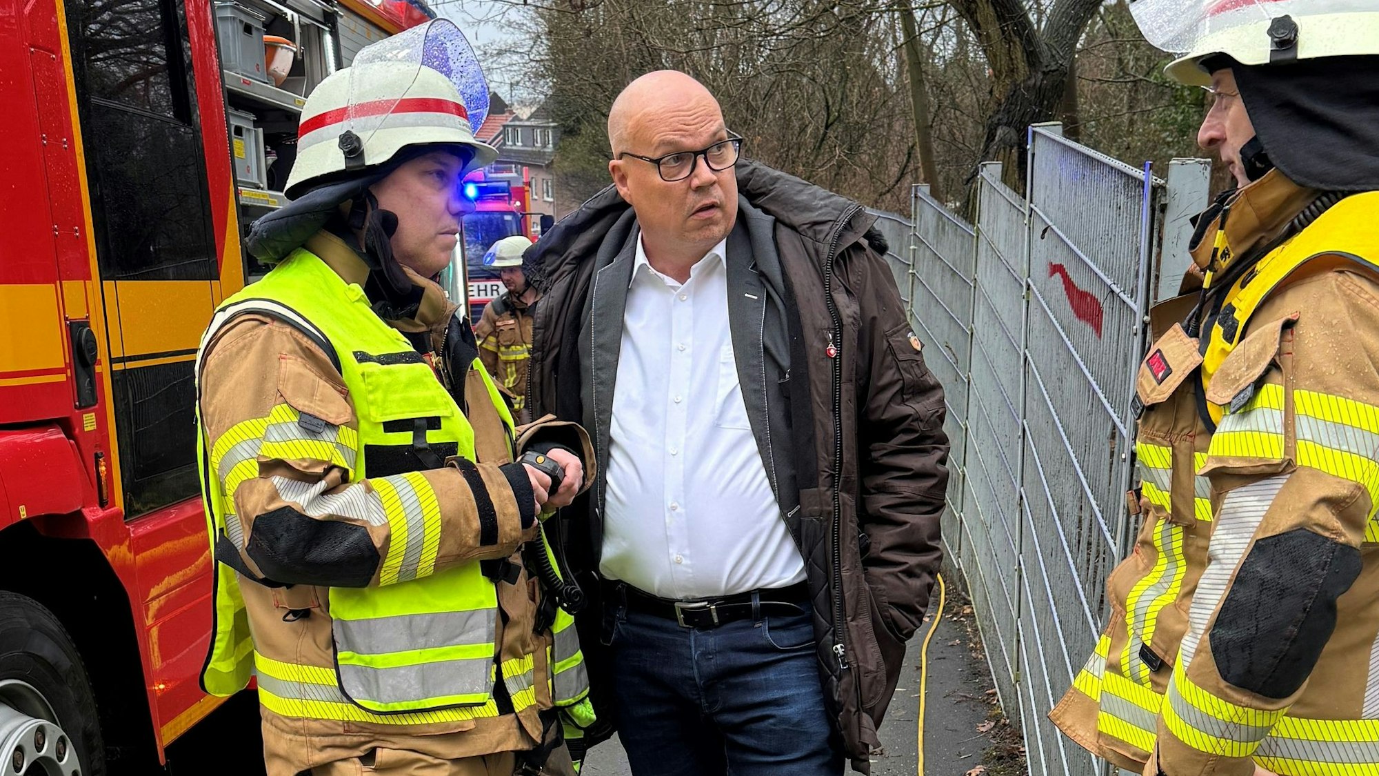 Auf dem Bild ist ein Mann im Gespräch mit zwei Feuerwehrmännern zu sehen.