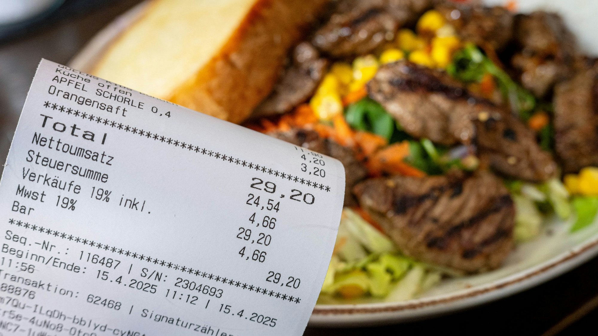 Eine Rechnung der Mehrwertsteuer neben einem vollen Teller in einem Restaurant.