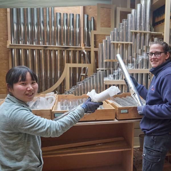 Zwei Handwerkerinnen halten Orgelpfeifen in den Händen.