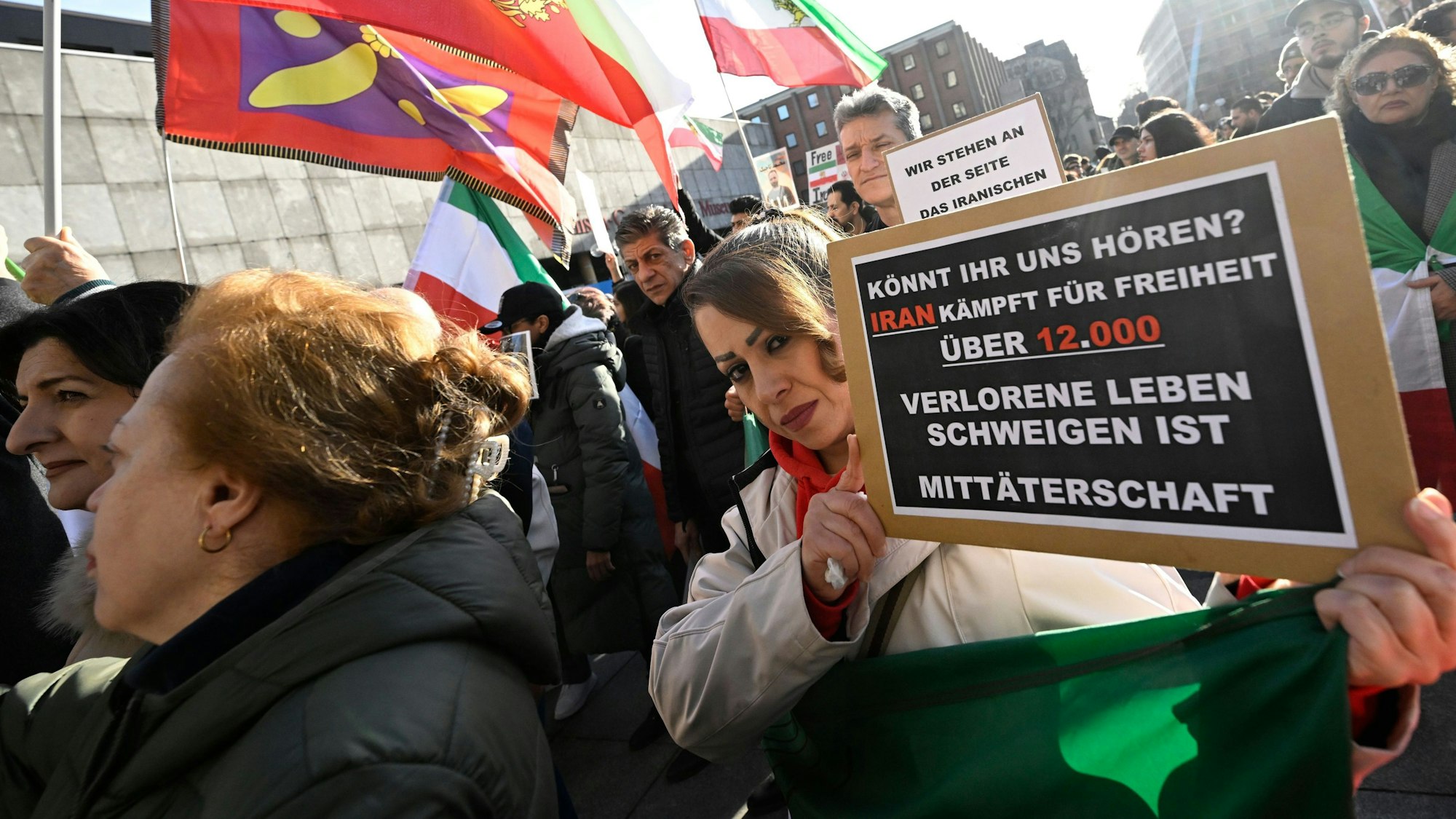 Teilnehmerinnen und Teilnehmer halten bei einer Demonstration Schilder und Fahnen zur Unterstützung der Proteste im Iran.