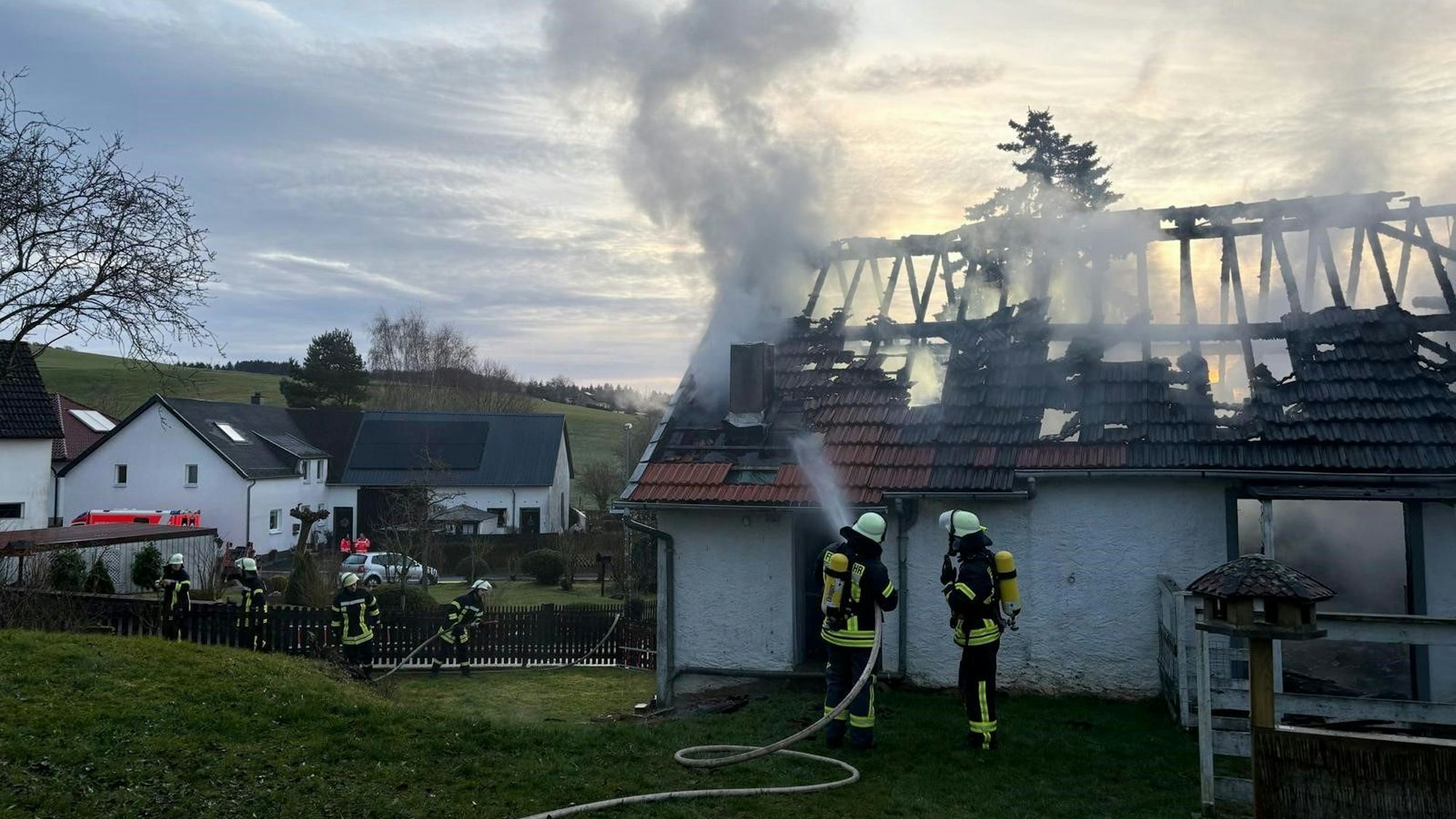 Aus der vom Feuer stark beschädigten Scheune steigt Rauch auf, Feuerwehrleute sind mit den Löscharbeiten beschäftigt.