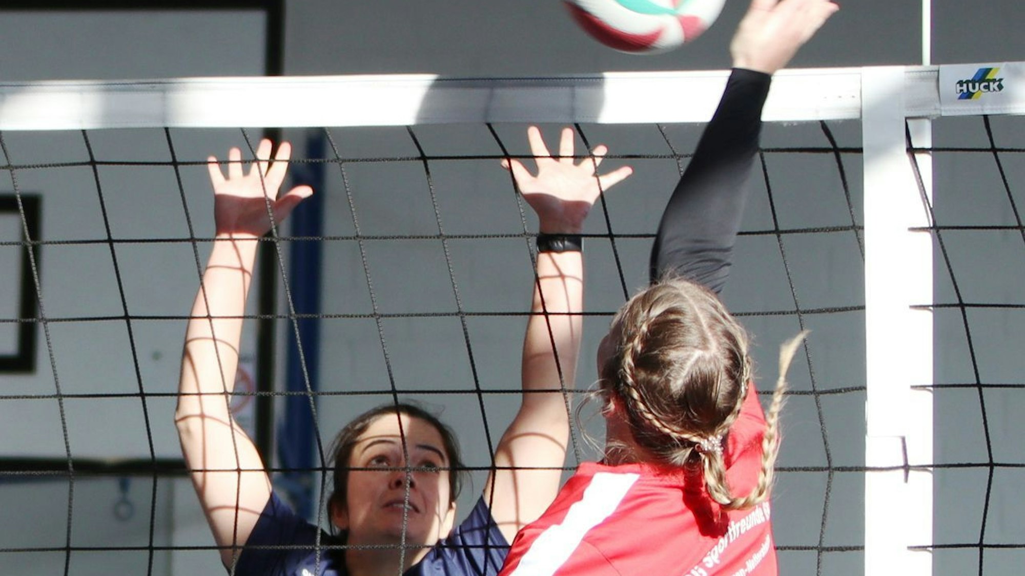 Das Bild zeigt zwei Spielerinnen, die sich am Netz duellieren.