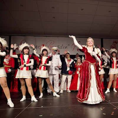 Prinzessin Emily I., die neue Tollität der Löstige Bröder Kall, winkt strahlend von der Bühne ins Publikum. Hinter ihr stehen die Tänzerinnen der Kallbachmücken in ihrem Ornat.