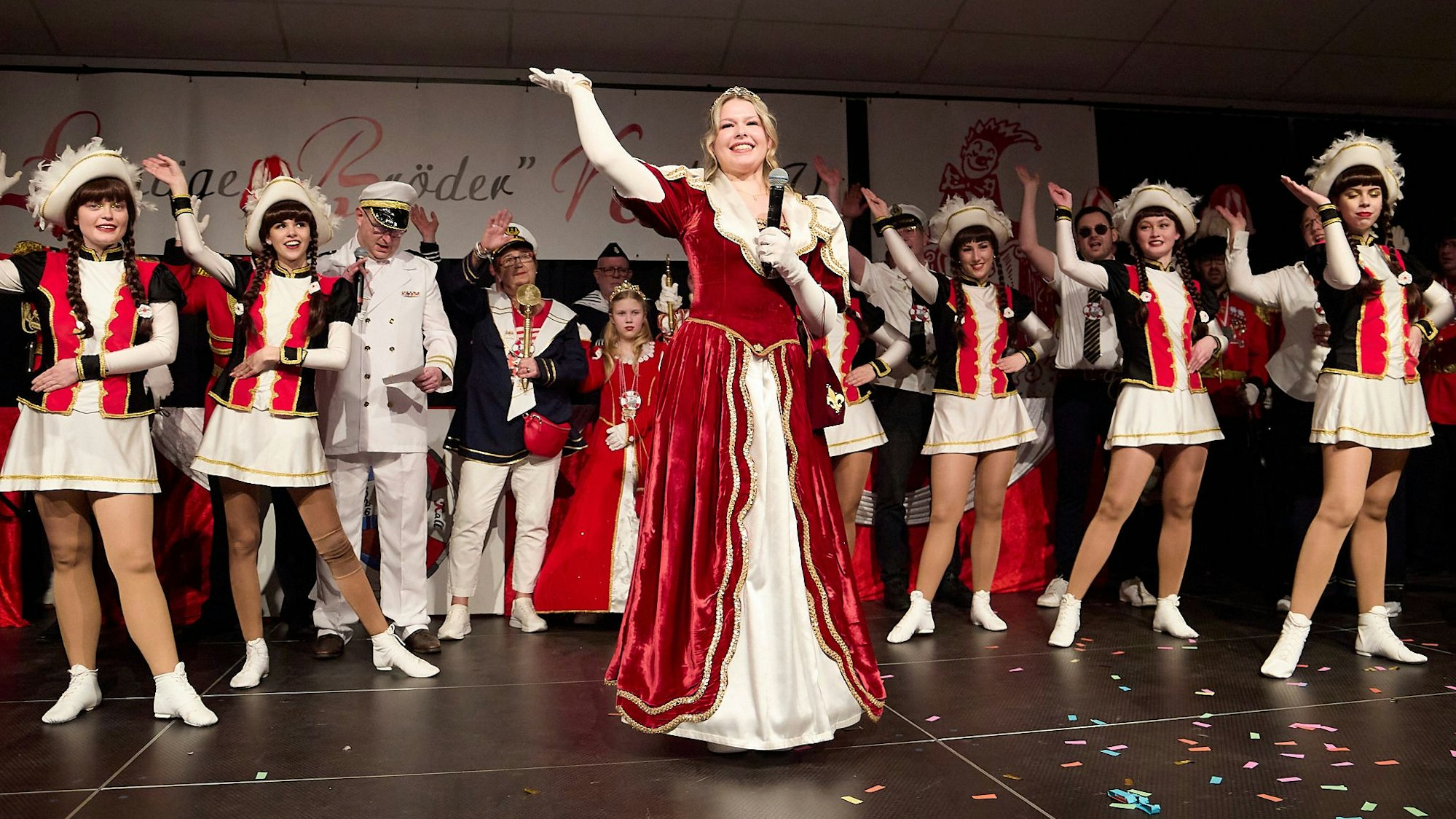 Prinzessin Emily I., die neue Tollität der Löstige Bröder Kall, winkt strahlend von der Bühne ins Publikum. Hinter ihr stehen die Tänzerinnen der Kallbachmücken in ihrem Ornat.