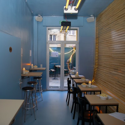 Ein Blick ins Lokal auf Hinterhof durchs Fenster sowie Holztische mit Kerzen drauf im Innenraum bei der Eröffnung des Wallczka-Bistro in der Kyffhäuserstrasse 50.