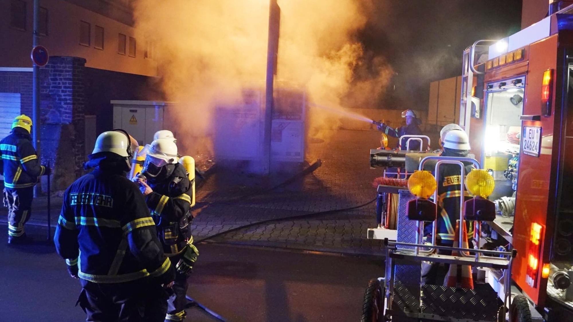 Feuerwehrleute löschen einen Kleidercontainer, der kräftig qualmt.