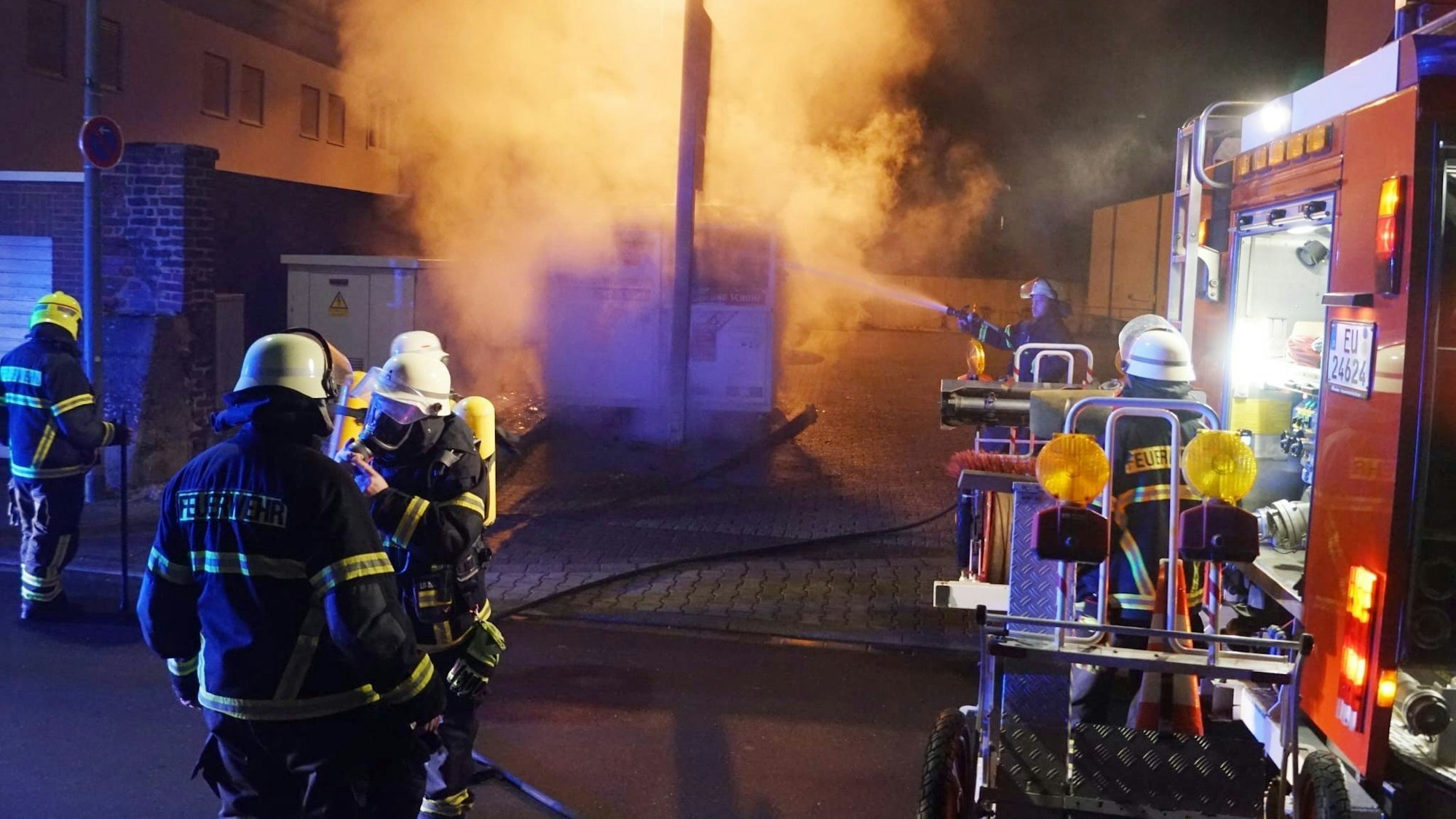 Feuerwehrleute löschen einen Kleidercontainer, der kräftig qualmt.