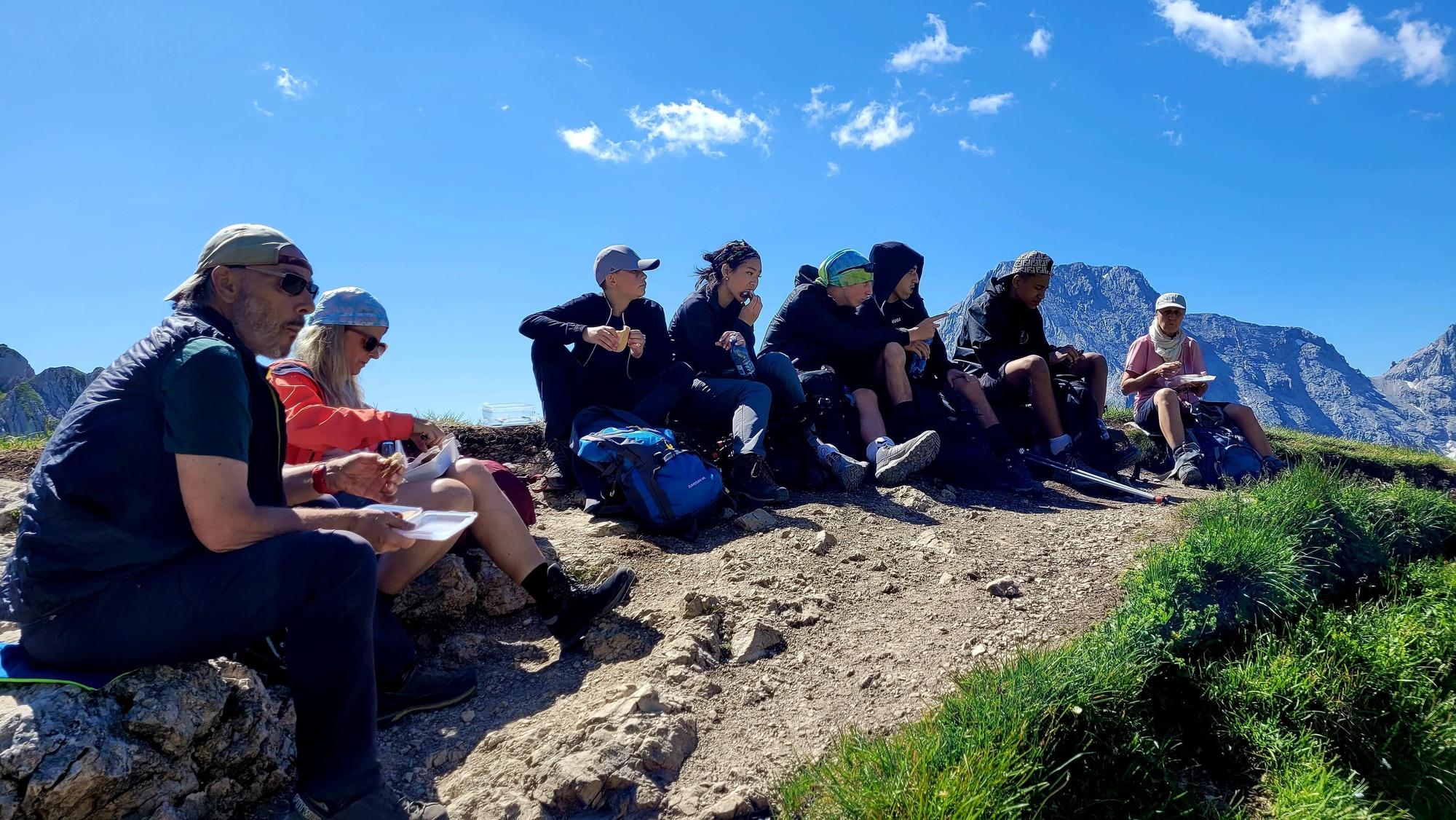 Eine Gruppe von Schülern macht eine Pause vor einem Bergpanorama.
