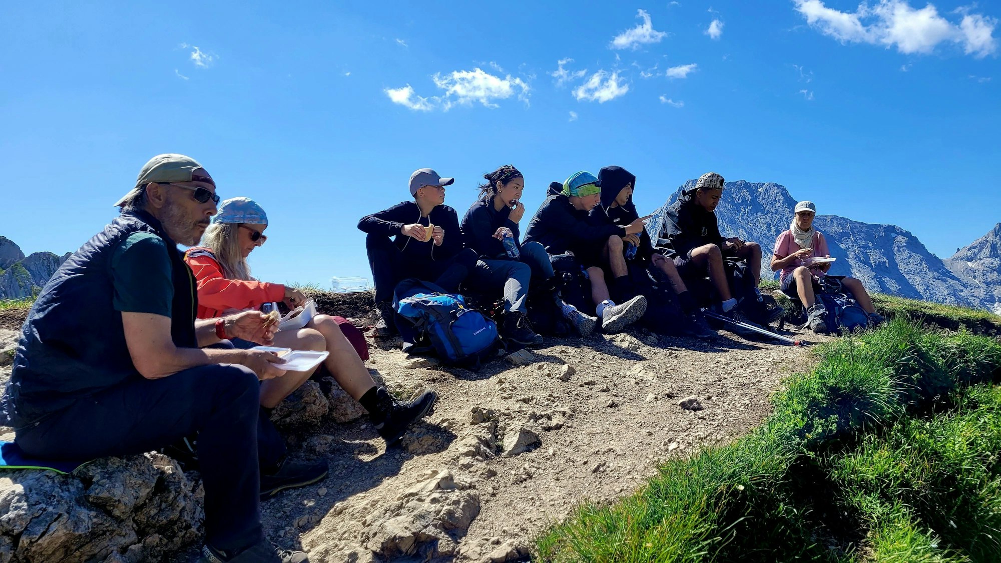 Eine Gruppe von Schülern macht eine Pause vor einem Bergpanorama.