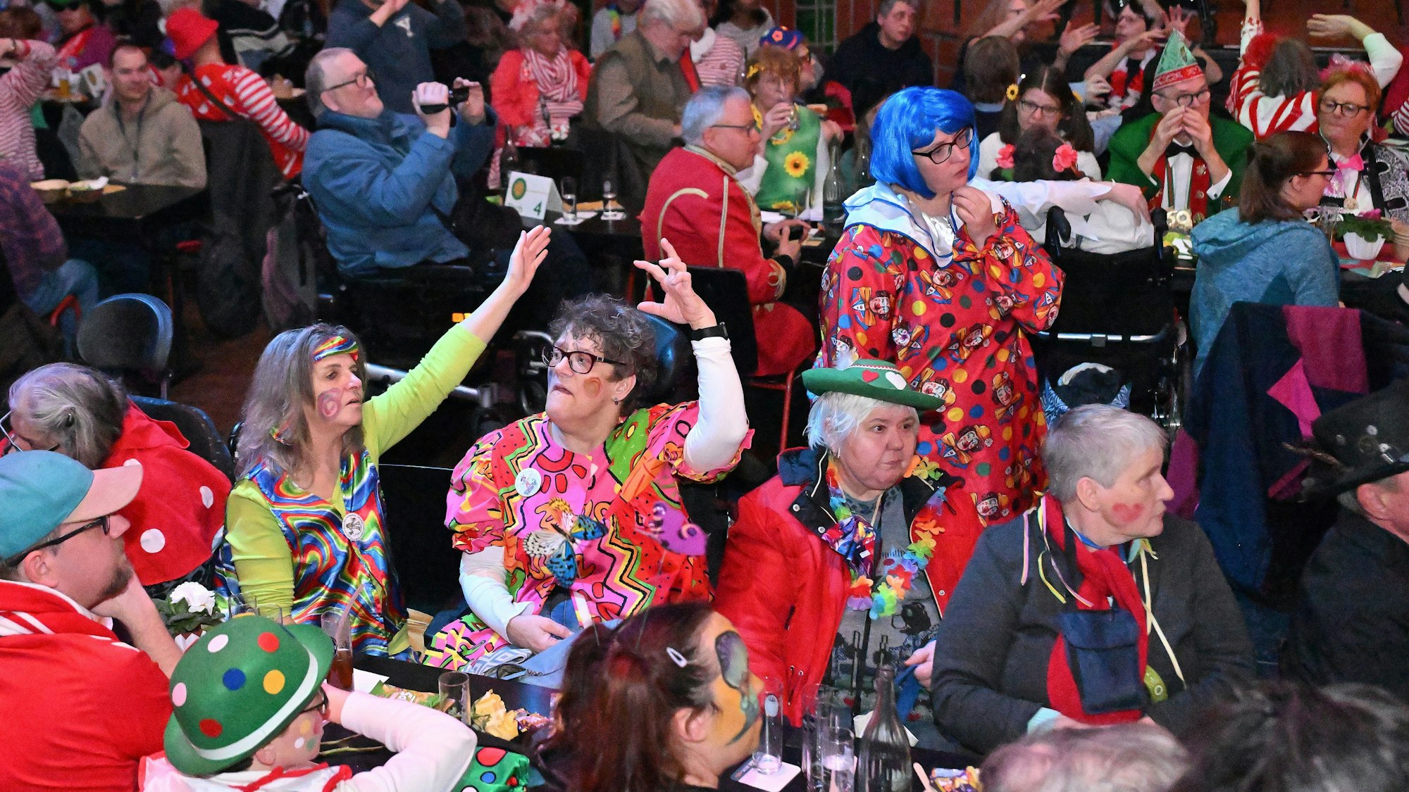 Bunt verkleidete Menschen sitzen im Publikum und winken mit den Armen.