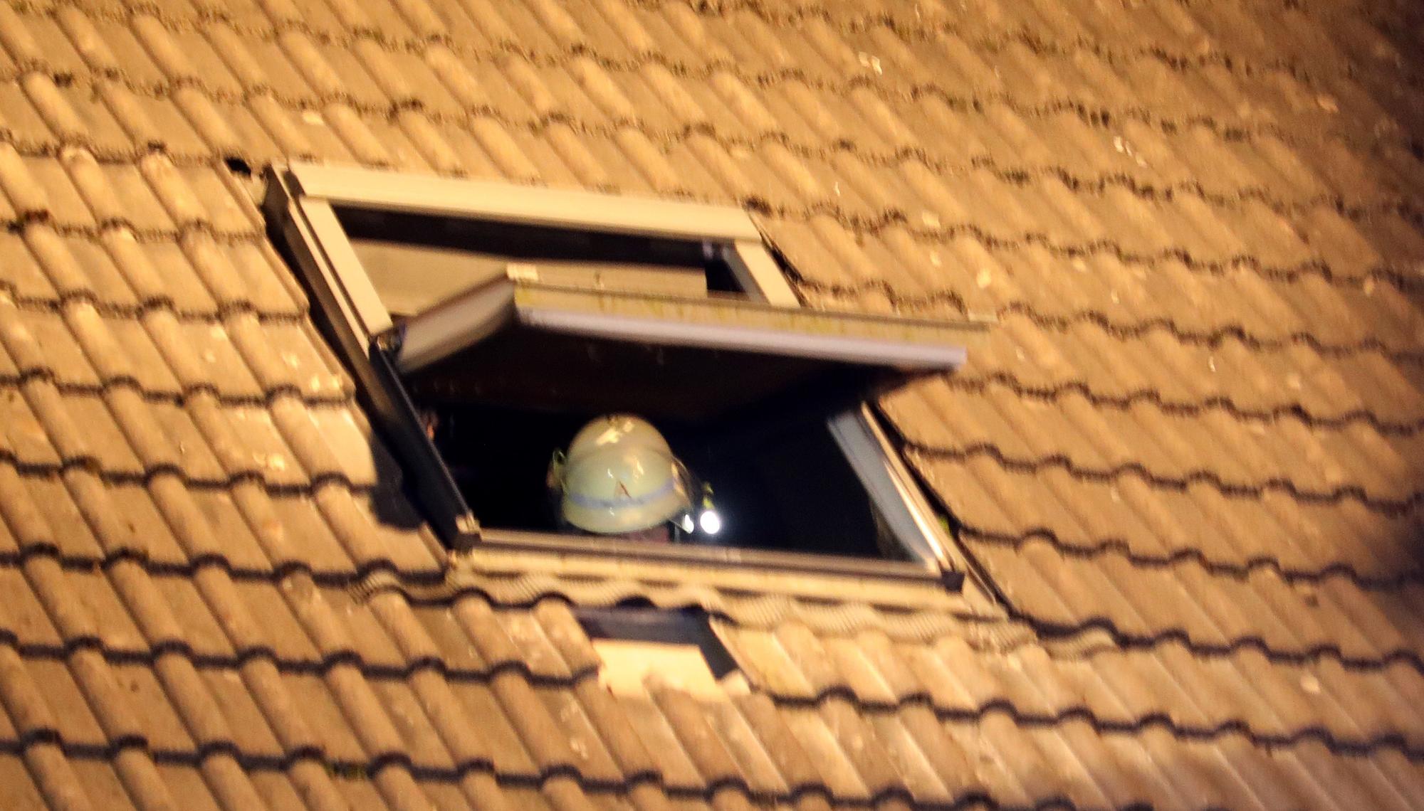 In einem Dachfenster ist der Helm eines Feuerwehrmanns zu sehen.