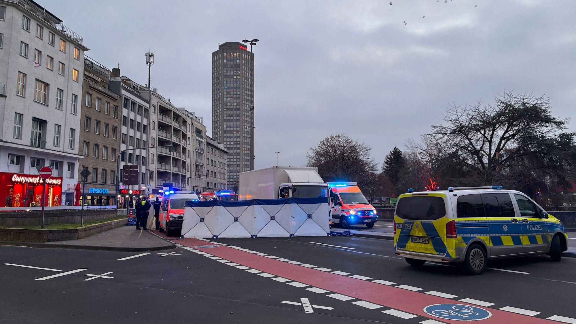 Die Polizei hat auf einer Fahrbahn einen Sichtschutz errichtet, davor stehen ein Lkw sowie Einsatzfahrzeuge von Polizei und Rettungsdienst.