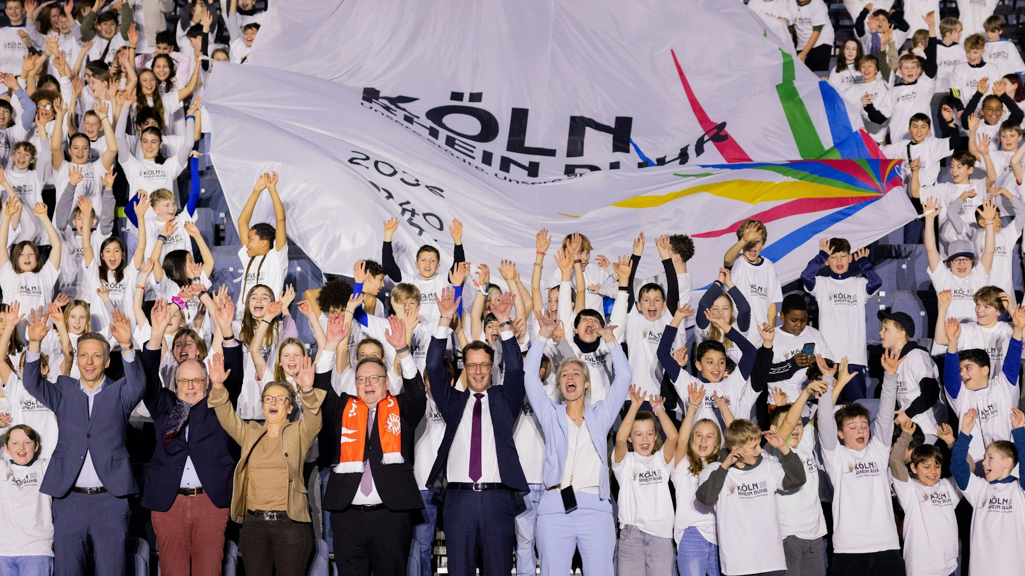 Auftakt der Olympia-Werbekampagne in der Kölner Lanxess-Arrena: NRW-Ministerpräsident Hendrik Wüst (CDU) und die Botschafter der Olympia-Bewerbung jubeln gemeinsam mit den Kindern einer Kölner Schule.