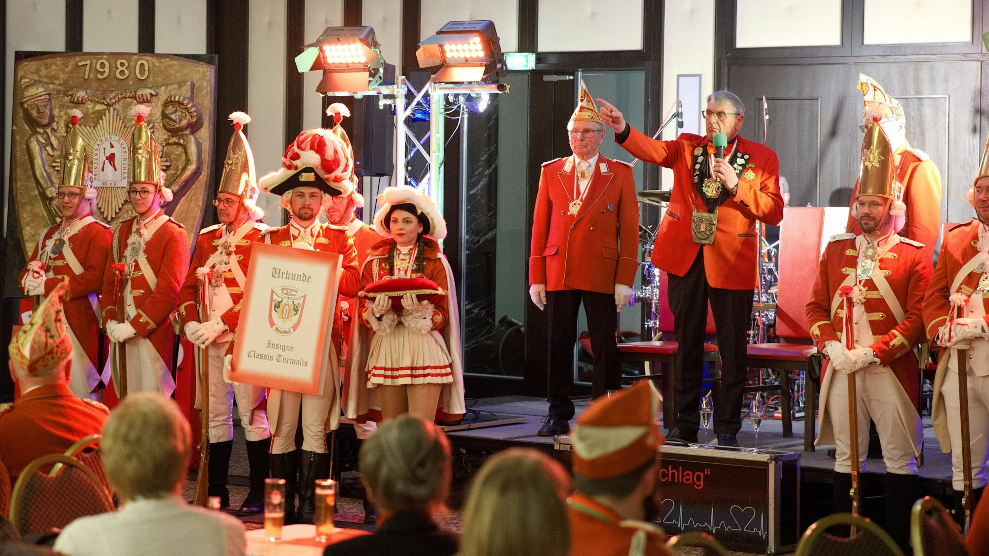 Der Ordensempfänger der„Insigne Classis Turmalis“ der Euskirchener Prinzengarde, Peter Barth, spricht im Saal zu einem Publikum. Er trägt einen Anzug und mehrere Karnevalsorden.