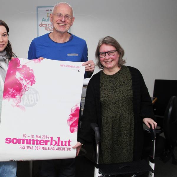 Zwei Frauen und ein Mann stehen nebeneinander. Der Mann hält ein Plakat, auf dem „Sommerblut“ zu lesen ist.