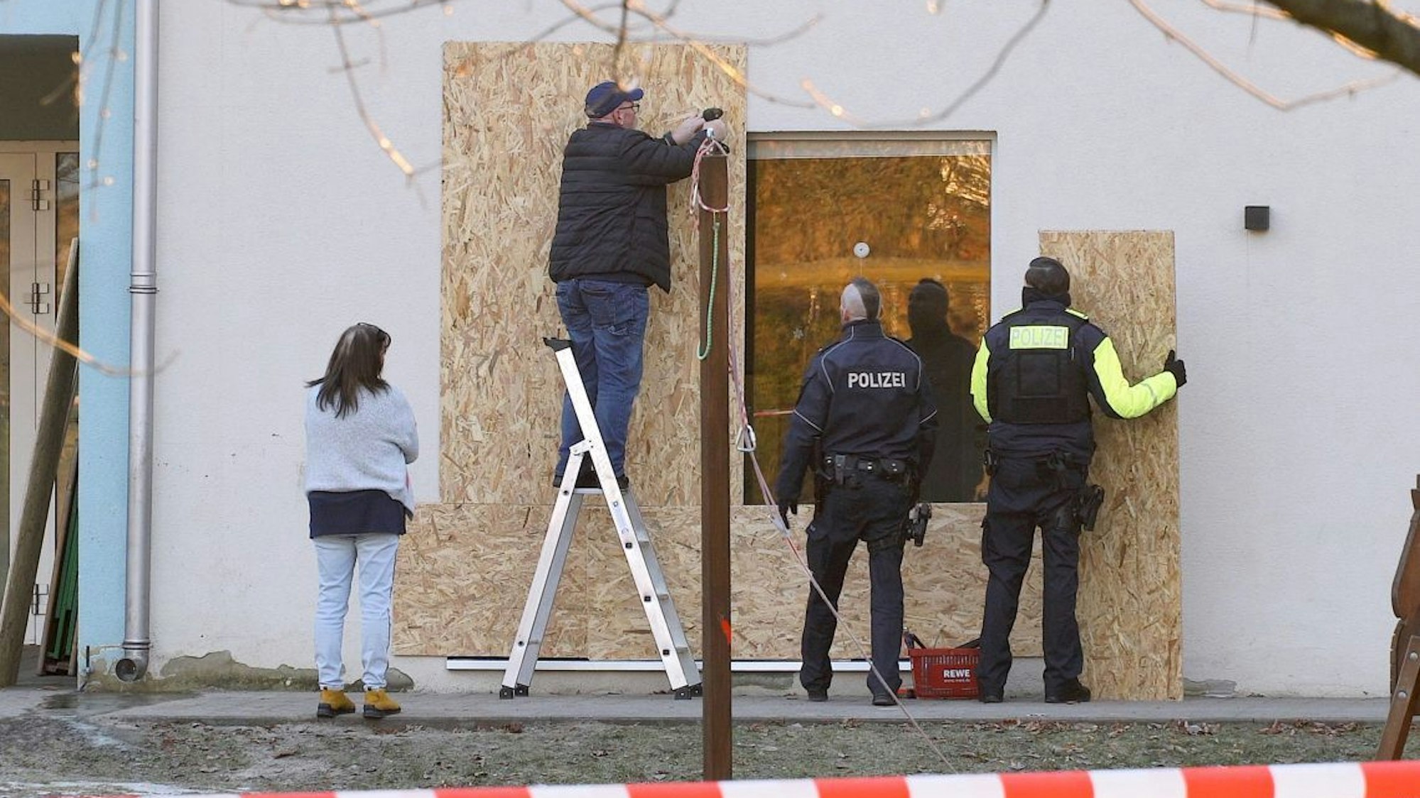 Vor einer beschädigten Terrassentür einer Kindertagesstätte in Niederschöneweide werden Holzplatten angebracht.