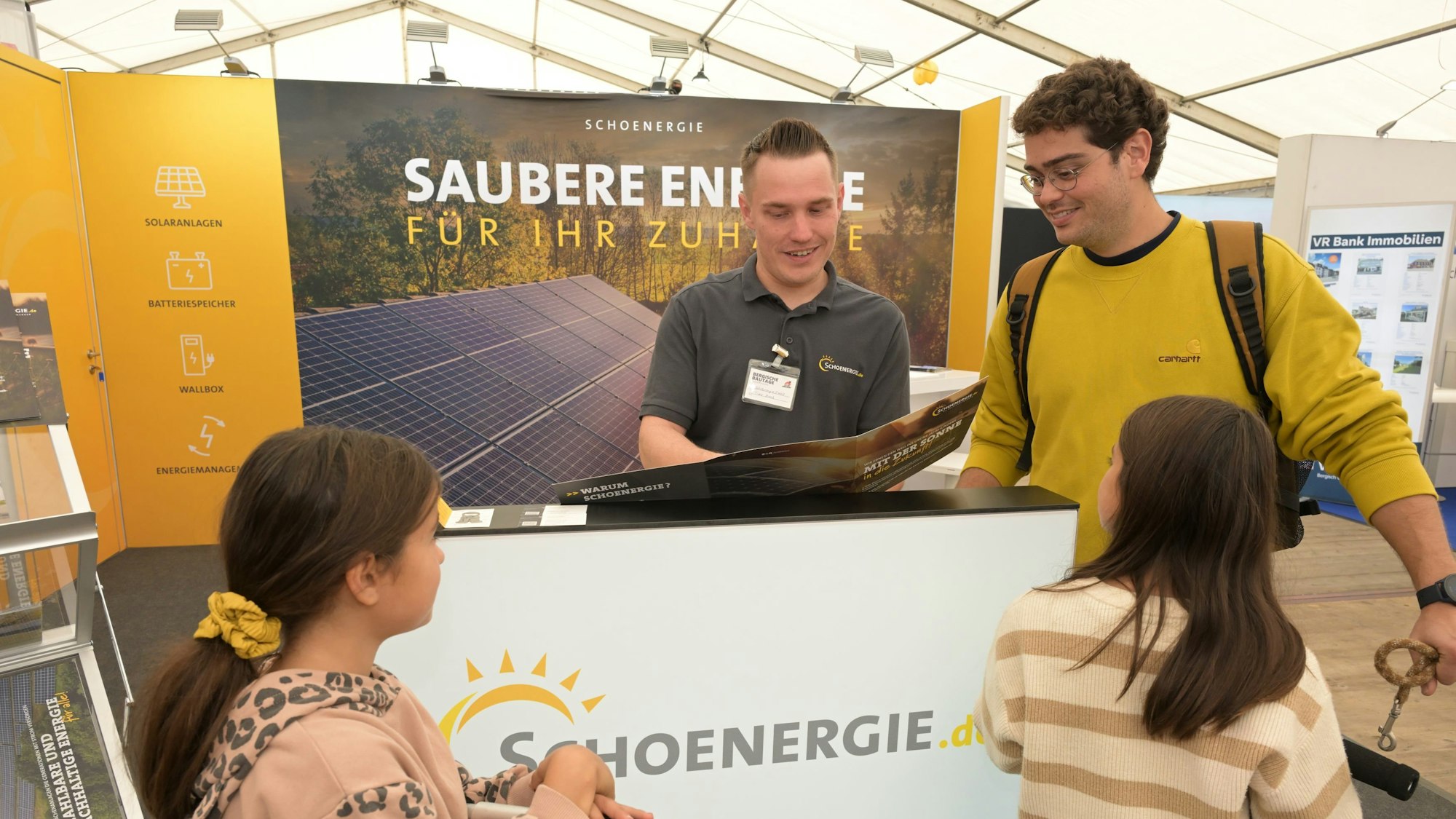 Zwei Männer stehen nebeneinander, während der eine dem anderen etwas in einem Prospekt zeigt. Sie befinden sich an einem Messestand.