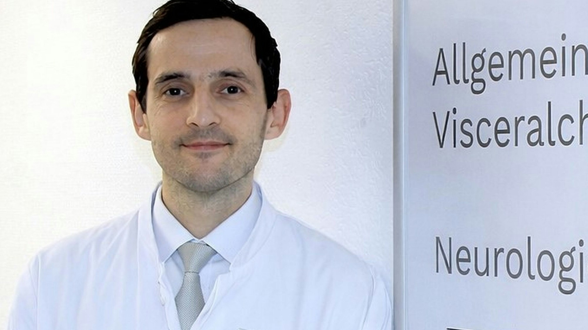 Auf dem Bild ist ein Portrait des neuen Chefarztes im Arztkittel im Krankenhaus zu sehen.