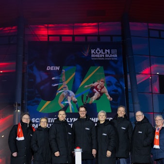 Acht Menschen stehen nebeneinander hinter einem Buzzer.