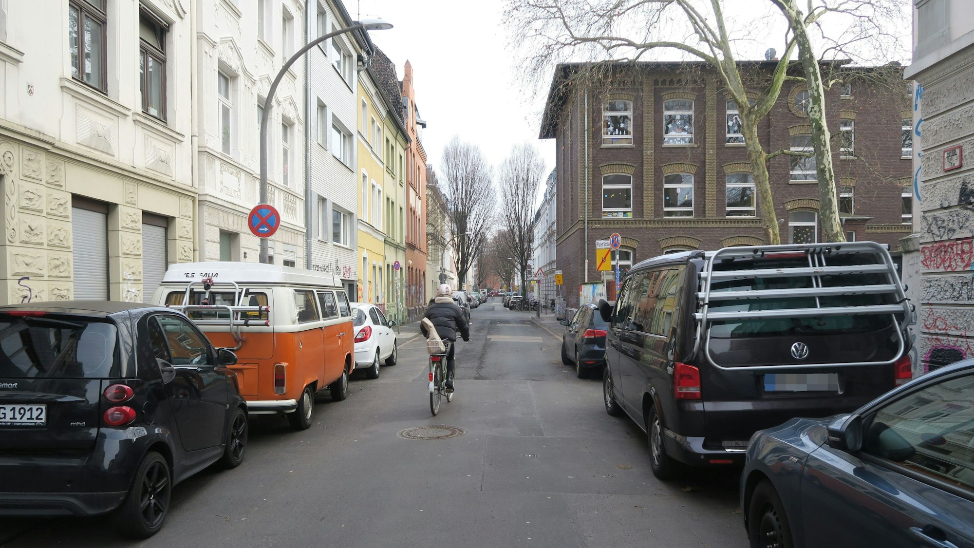 Ein Radfahrer ist auf einer schmalen Straße unterwegs, links und rechts am Fahrbahnrand stehen Autos.