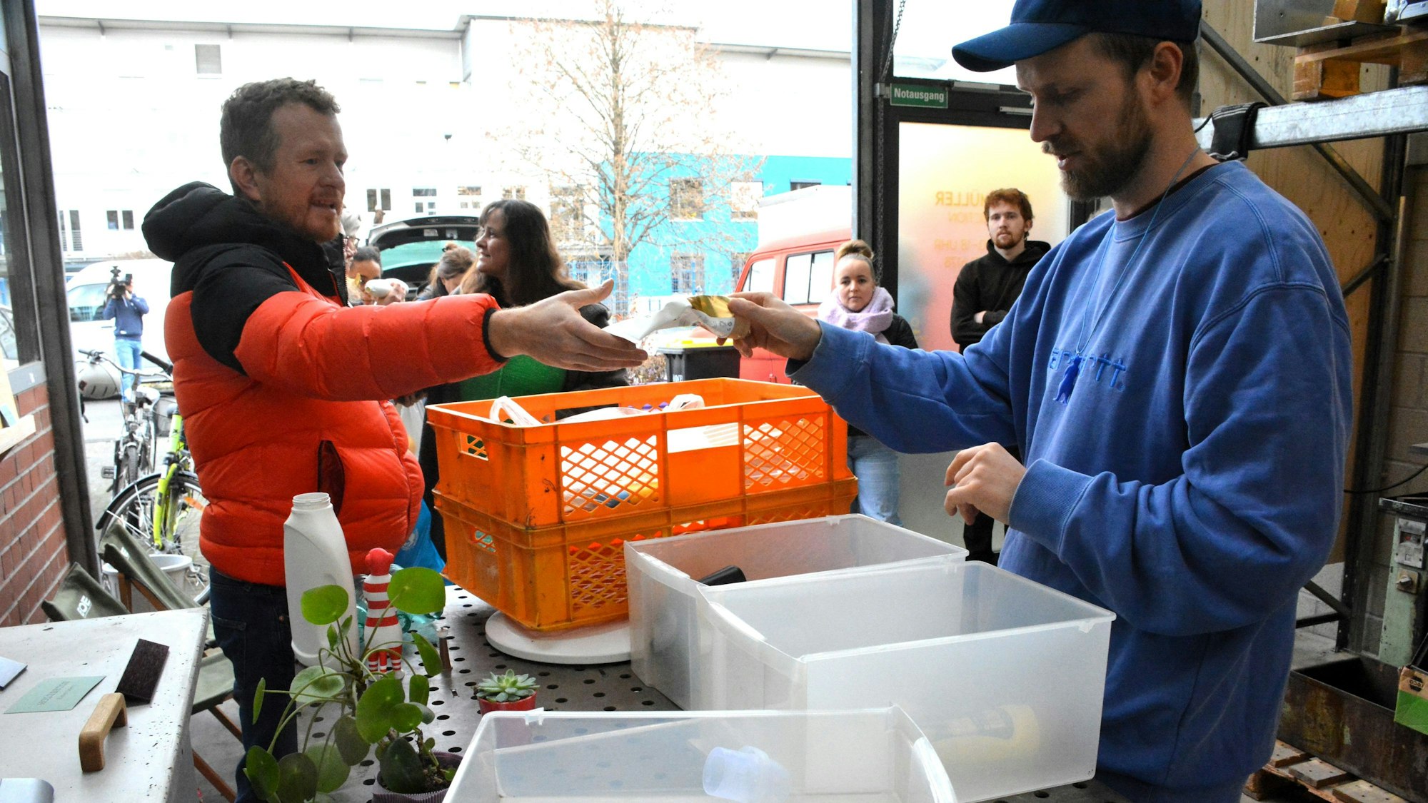 Ein Mann überreicht einem zweiten eine leere Plastikflasche
