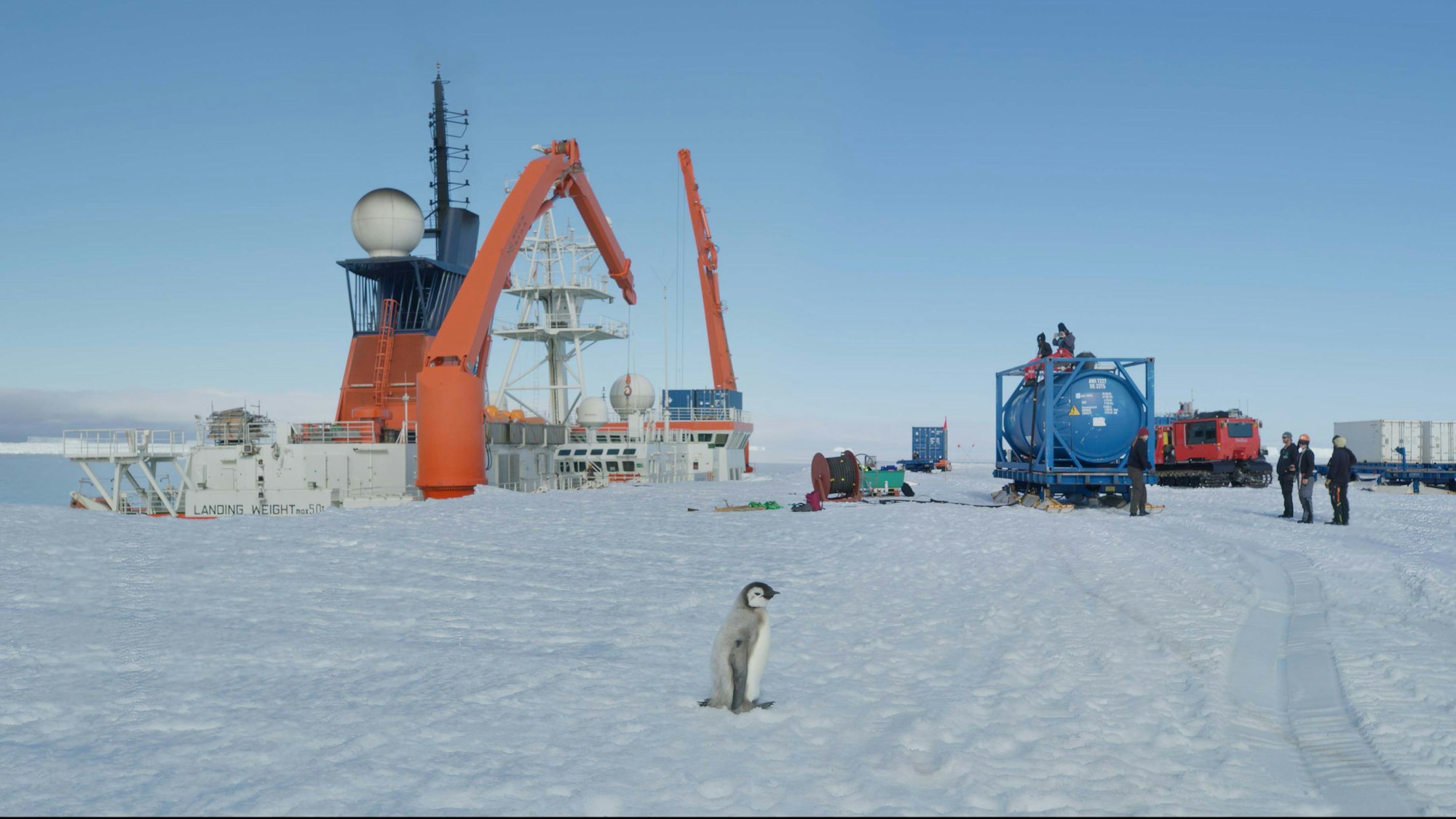 Ein Pinguin steht im Schnee vor einer Industrieanlage