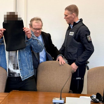 Der Angeklagte mit seinem Verteidiger Lukas Pieplow und einem Wachtmeister beim Prozessauftakt im Kölner Landgericht.