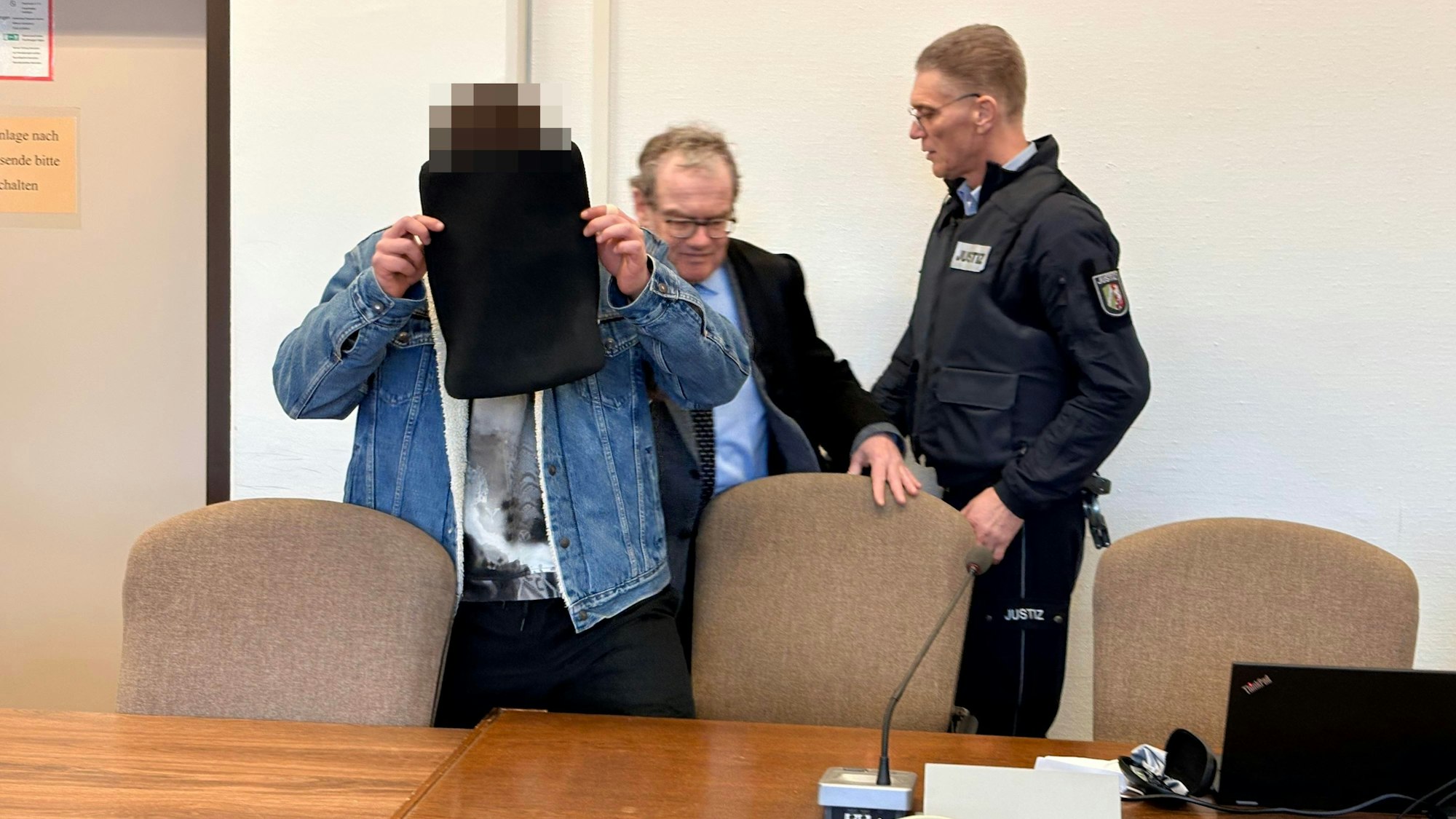 Der Angeklagte mit seinem Verteidiger Lukas Pieplow und einem Wachtmeister beim Prozessauftakt im Kölner Landgericht.