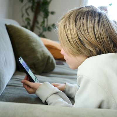 Das Bild zeigt einen Jungen, der auf einem Sofa und guckt auf sein Smartphone. (gestellte Szene). Australien hat vor rund einem Monat ein Social-Media-Verbot für Kinder und Jugendliche unter 16 Jahren eingeführt und ist damit weltweiter Vorreiter.