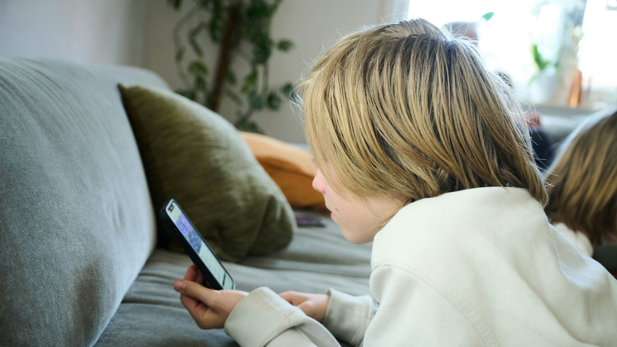 Das Bild zeigt einen Jungen, der auf einem Sofa und guckt auf sein Smartphone. (gestellte Szene). Australien hat vor rund einem Monat ein Social-Media-Verbot für Kinder und Jugendliche unter 16 Jahren eingeführt und ist damit weltweiter Vorreiter.