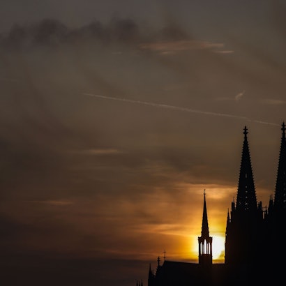 Die Sonne geht am Abend in Köln bei Schleierwolken hinter dem Dom unter.