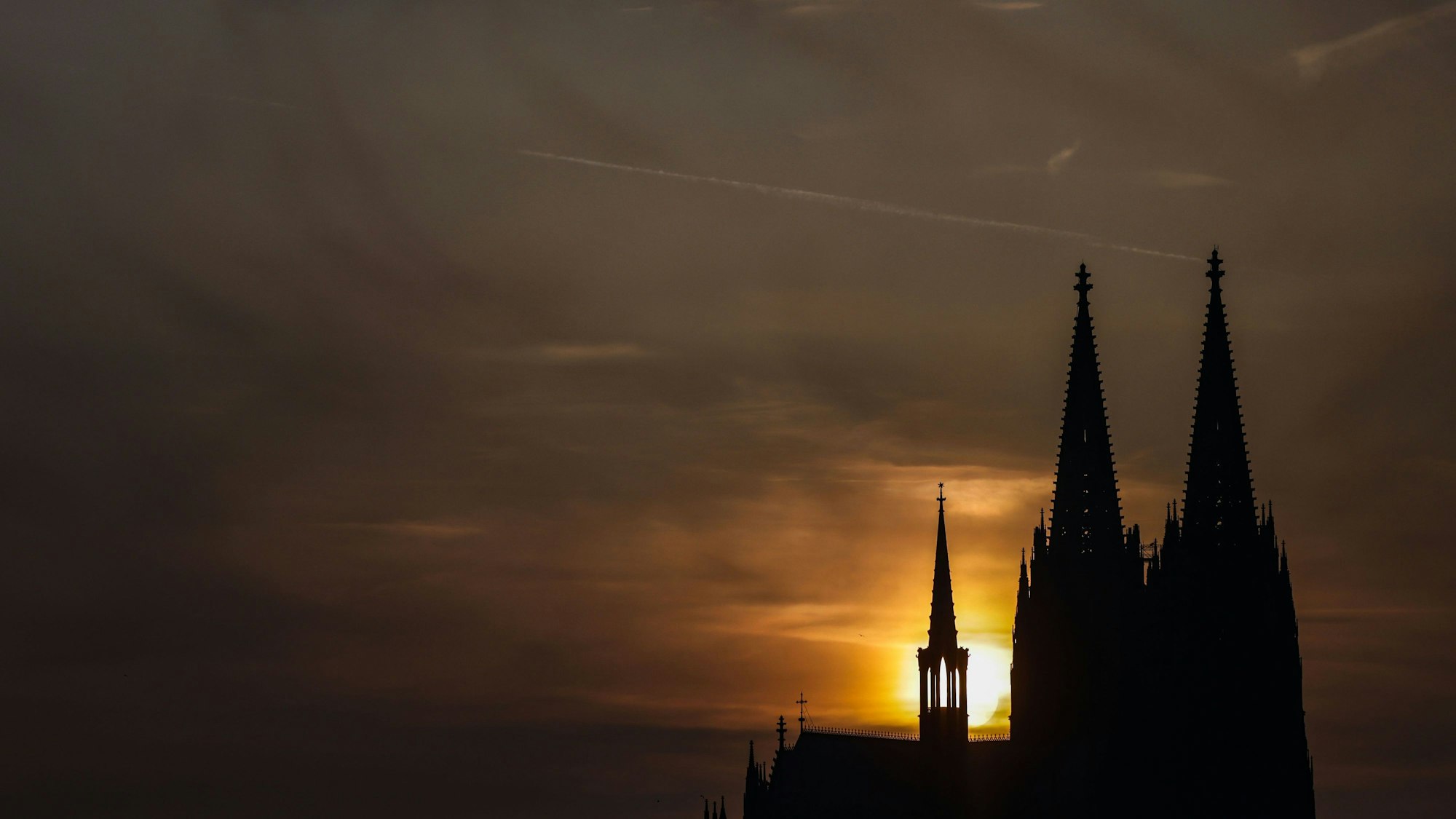 Die Sonne geht am Abend in Köln bei Schleierwolken hinter dem Dom unter.