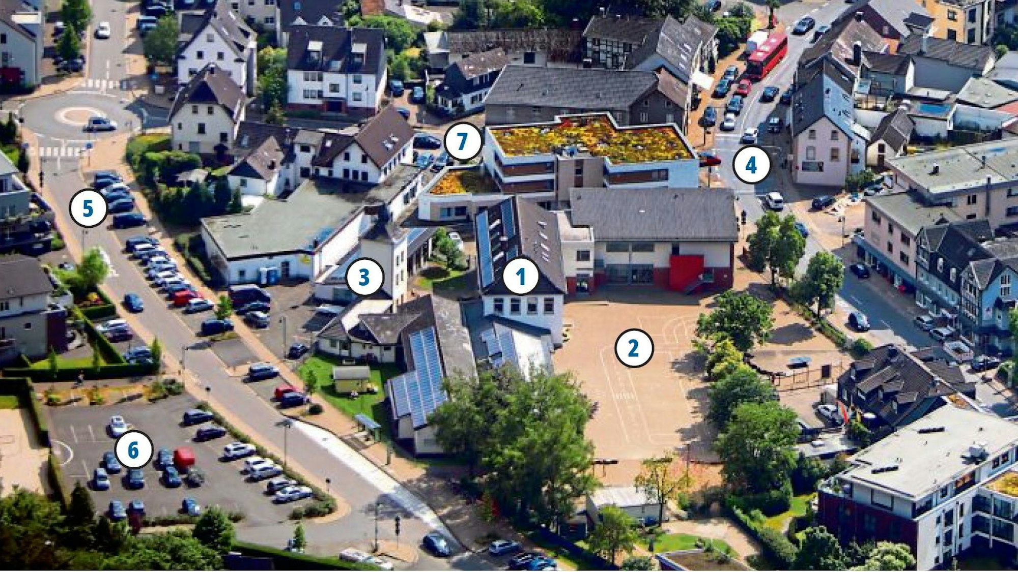 Eine Ansicht der von der Sonne beschienenen Ortsmitte von Hoffnungsthal aus der Vogelperspektive mit Schule, Schulhof, Freibad-Parkplatz und Hauptstraße.