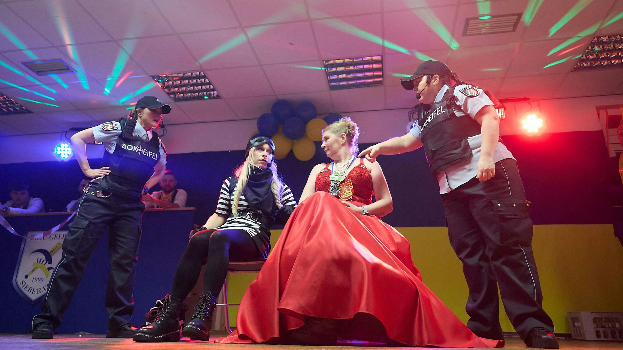 Eine als Prinzessin kostümierte Frau sitzt neben einer Frau, die als Räuberin verkleidet ist. Die beiden werden von Frauen in Polizistinnenkostümen flankiert.