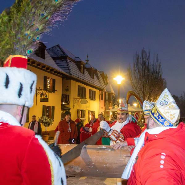 Zwei Männer in roten Mänteln zersägen einen Baumstamm.