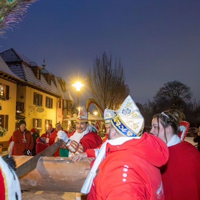 Zwei Männer in roten Mänteln zersägen einen Baumstamm.