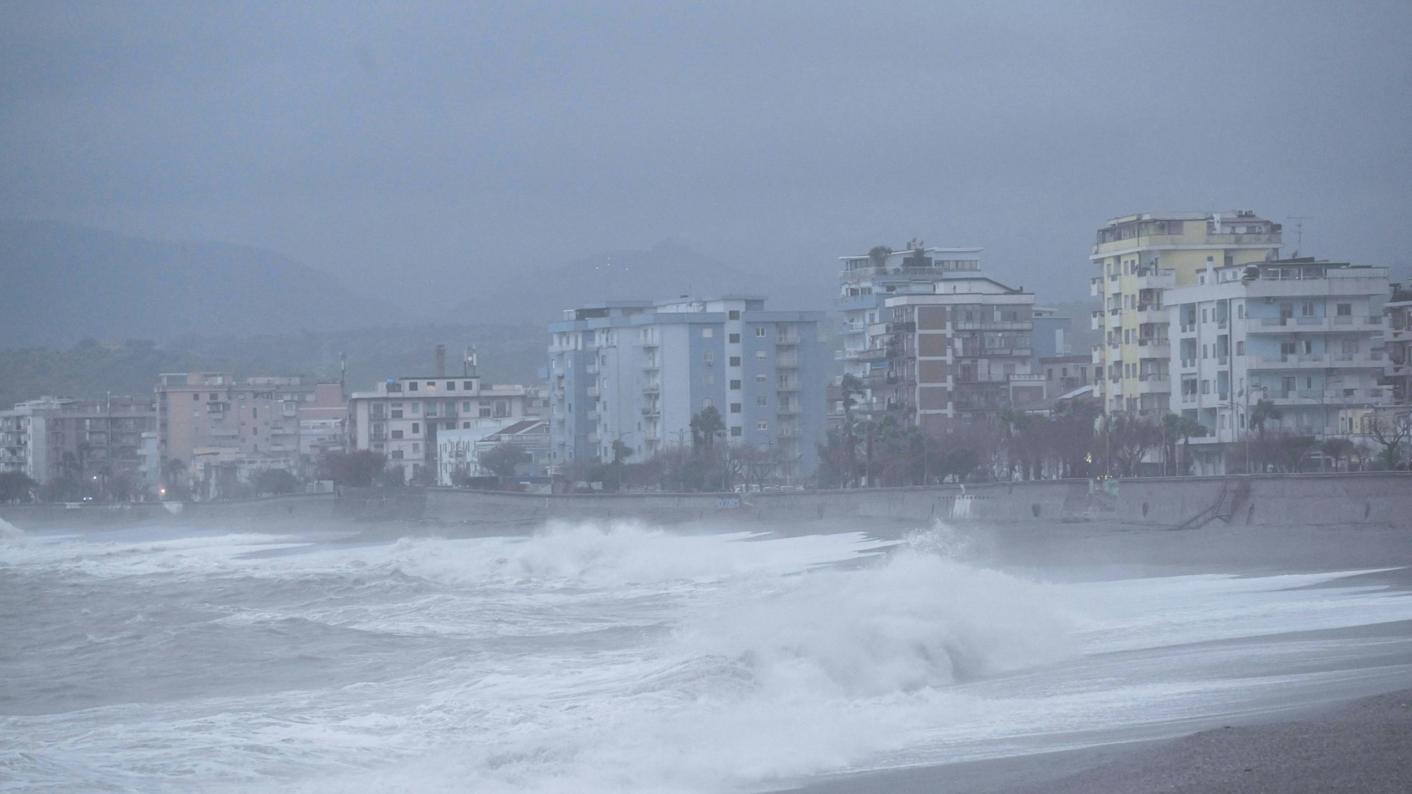 Küstenlandschaft mit hohen Wellen und Gebäuden.