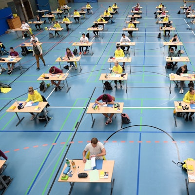 Schüler und Schülerinnen sitzen in einer Sporthalle und schreiben eine Abiturprüfung.