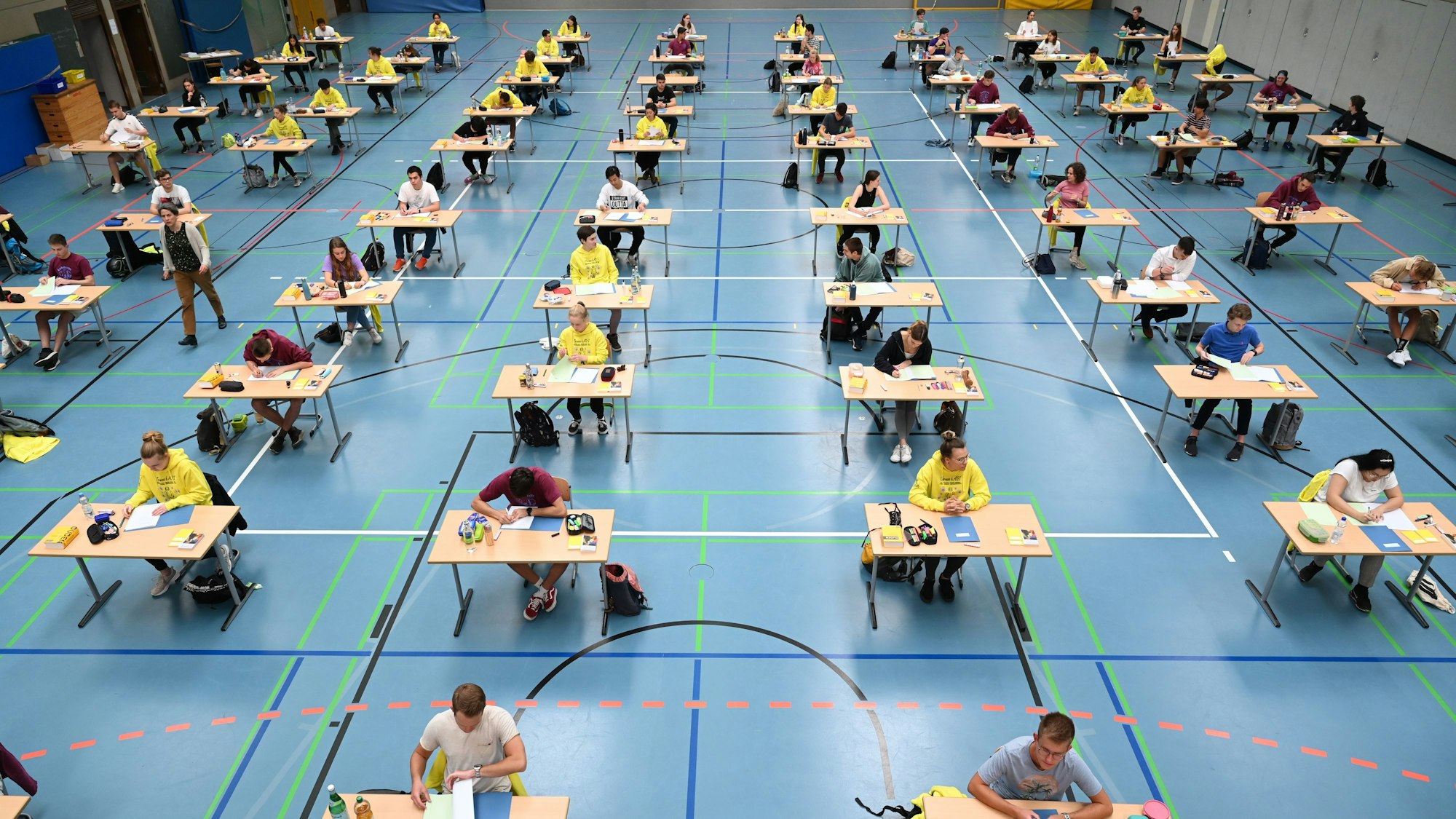 Schüler und Schülerinnen sitzen in einer Sporthalle und schreiben eine Abiturprüfung.