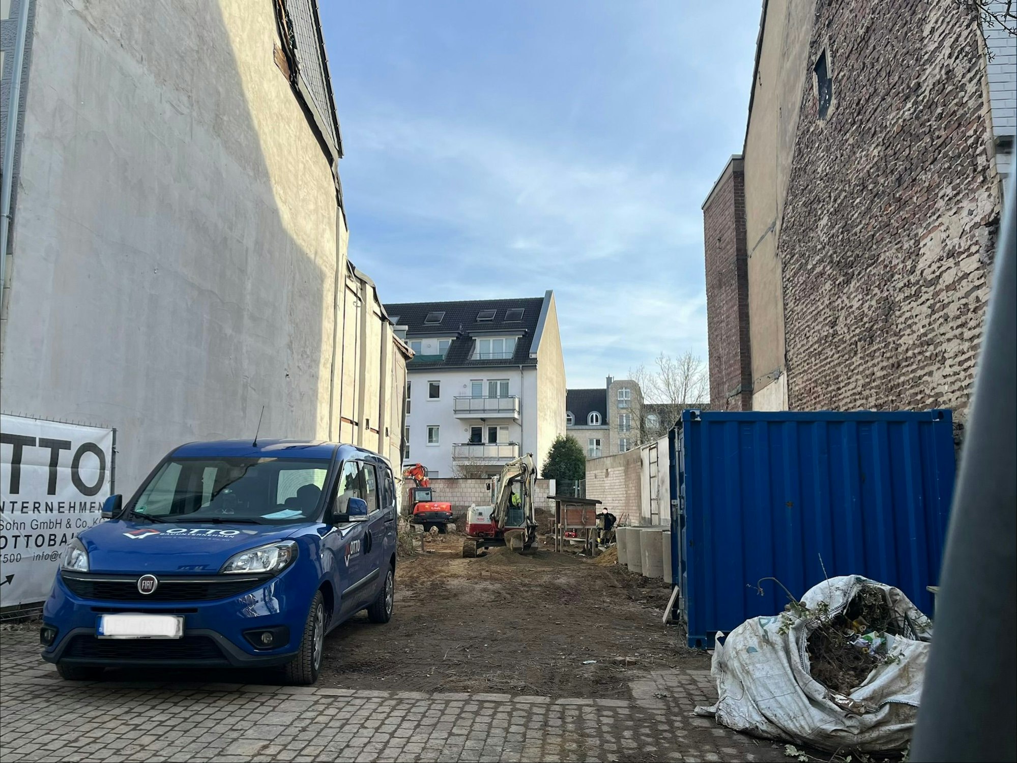 Durch Lücken im Bauzaun lässt sich ein kleiner Bagger bei der Arbeit beobachten.