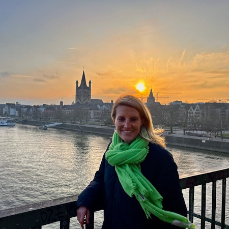 Eine Frau mit grünem Schal steht vor einem großen Schiff.