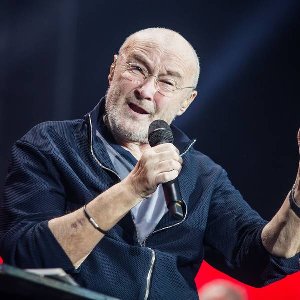 Sänger Phil Collins sitzt auf der Bühne und singt.