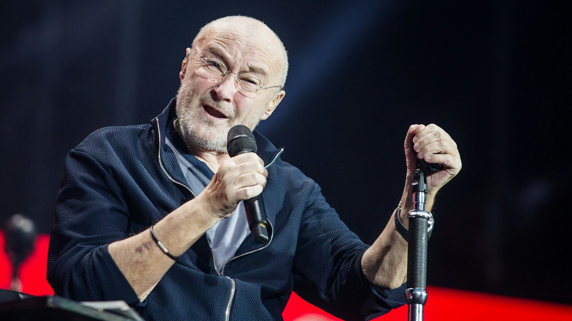 Sänger Phil Collins sitzt auf der Bühne und singt.