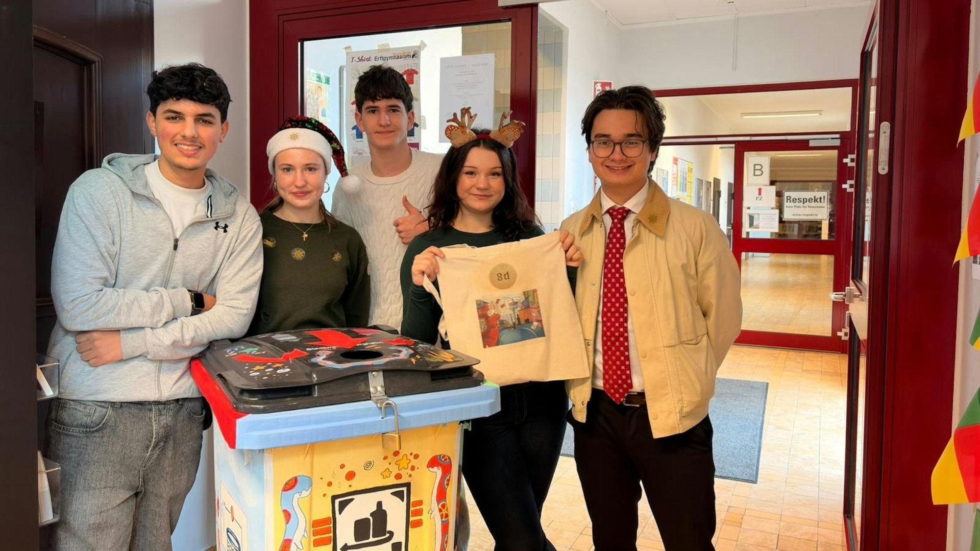 Vier Schülerinnen und Schüler stehen an der gestalteten Tonne, eine hält einen Jutebeutel hoch, mit dem eine Klasse das Pfand sammeln kann.