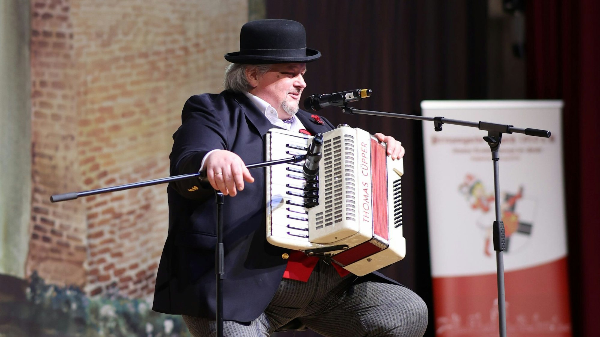 Thomas Cüpper trägt Anzug und Hut und hat ein Akkordeon vor die Brust geschnallt.
