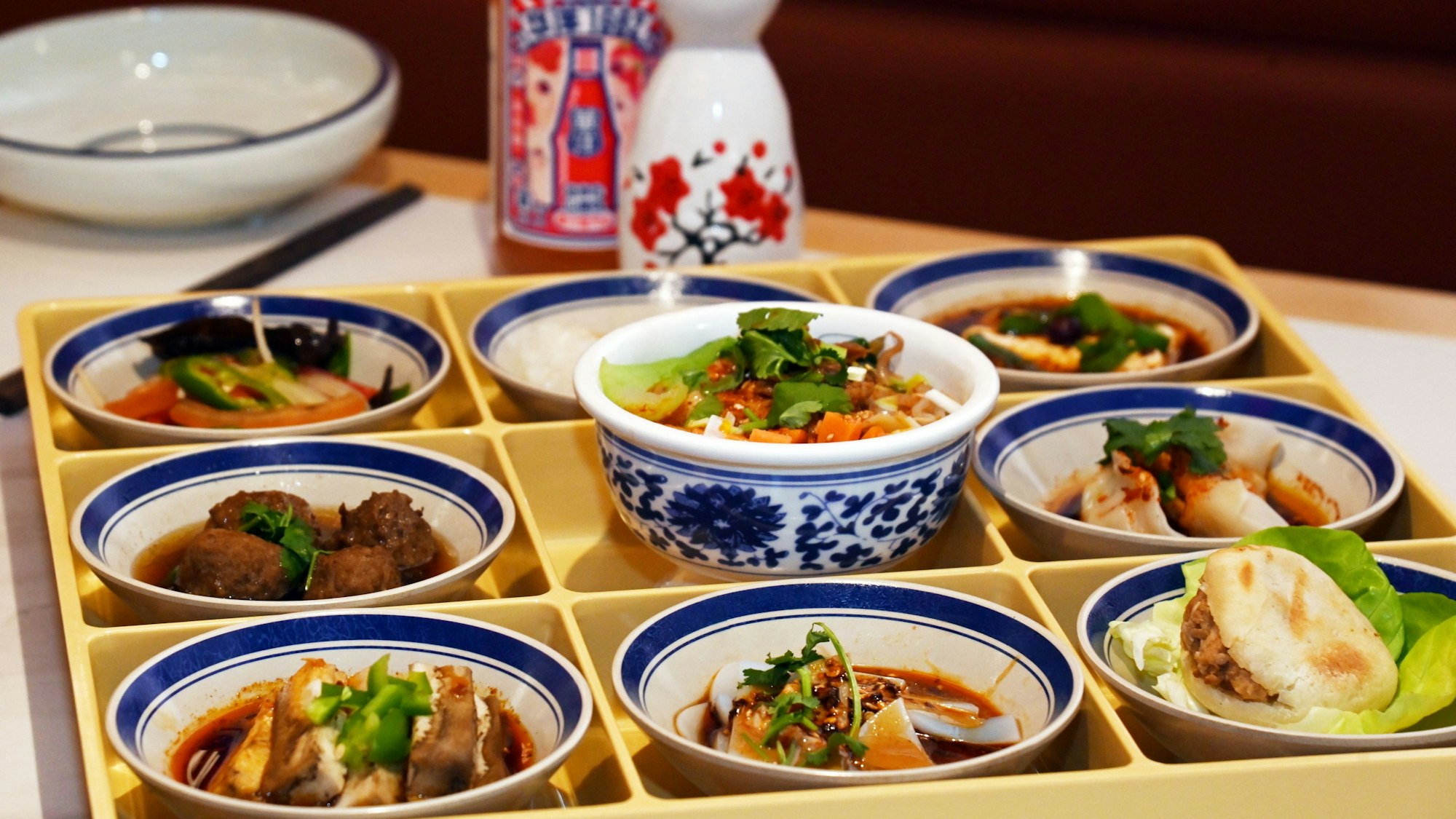 Ein Tablett mit neun Schälchen in Tablettkammern ist zu sehen. Darin die Speisen schön angerichtet.